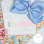 Floral Block Sketch Stitch Embroidery Font: The name Charlotte in pink floral sketch letters on a white shirt with a blue bow