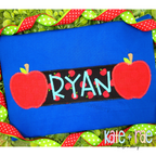 Apple Name Frame Zigzag Applique Embroidery Design: Red apple appliques framing the name RYAN in aqua on a black apple print name plate on a blue shirt