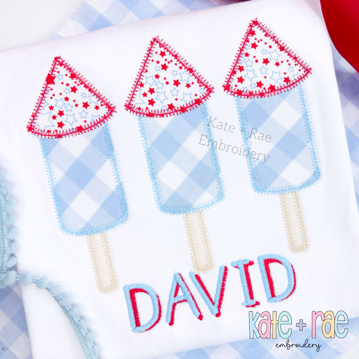 Boy's Firework Trio Zigzag Applique Embroidery Design: Three blue gingham firework rocket appliques with red star tops above the name DAVID in red on a white shirt