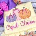 Girl's Fall Pumpkin Trio with Bows Sketch Stitch Machine Embroidery Design: Three sketch stitch pumpkins with pink bows above the name Cyril Claire in pink script on a yellow shirt