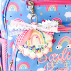 ITH Scalloped Circle Bag Tag Satin Stitch Applique Embroidery Design: Rainbow print backpack with a scalloped rainbow bag tag and the name Sadie Rae in pink