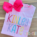 Summer Nights Satin Stitch Embroidery Font: The name Kinley Kate stitched in rainbow colored letters on a pink shirt with a hot pink bow