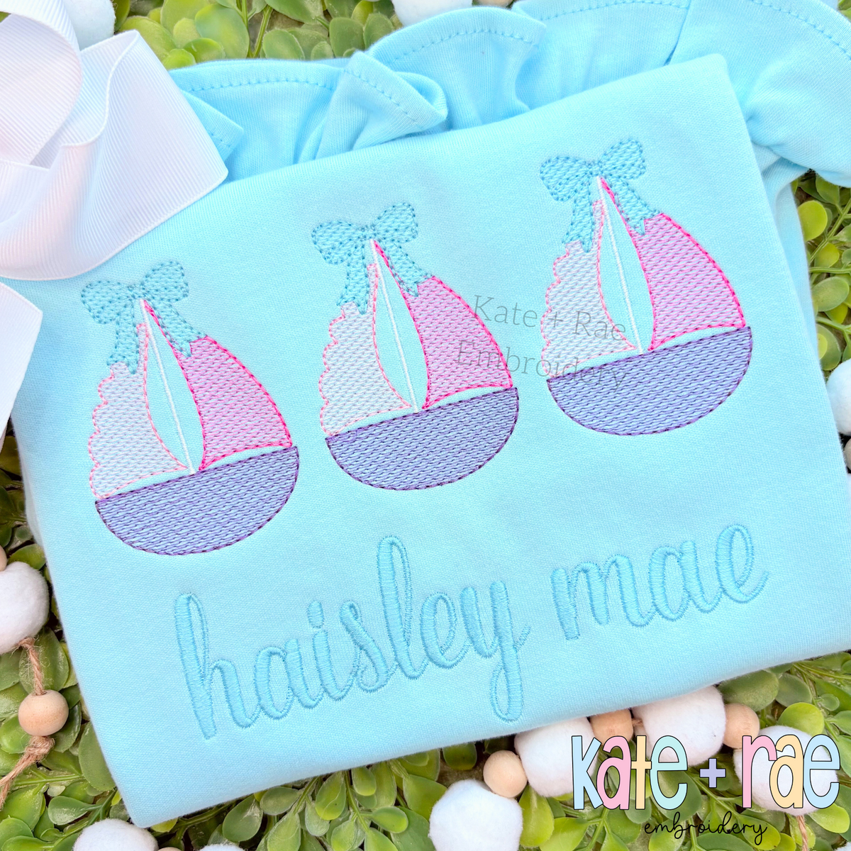 Sailboat Trio with Bows Sketch Stitch Embroidery Design: Three pink and purple sketch sailboats with bows above the name haisley mae on a light blue shirt