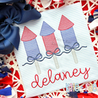 Girl's Firework Trio with Bows Sketch Stitch Embroidery Design: Three red and blue sketch firework rockets with navy bows above the name delaney in red script on a striped shirt