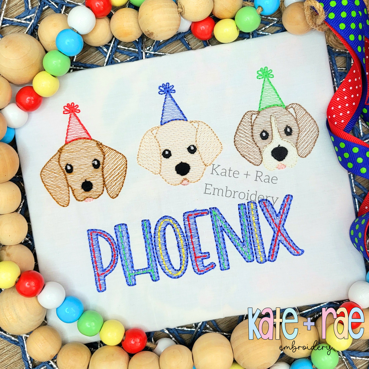 Birthday Puppies Trio Sketch Stitch Embroidery Design: Three puppy faces in party hats above the name Phoenix in blue and purple on a white shirt