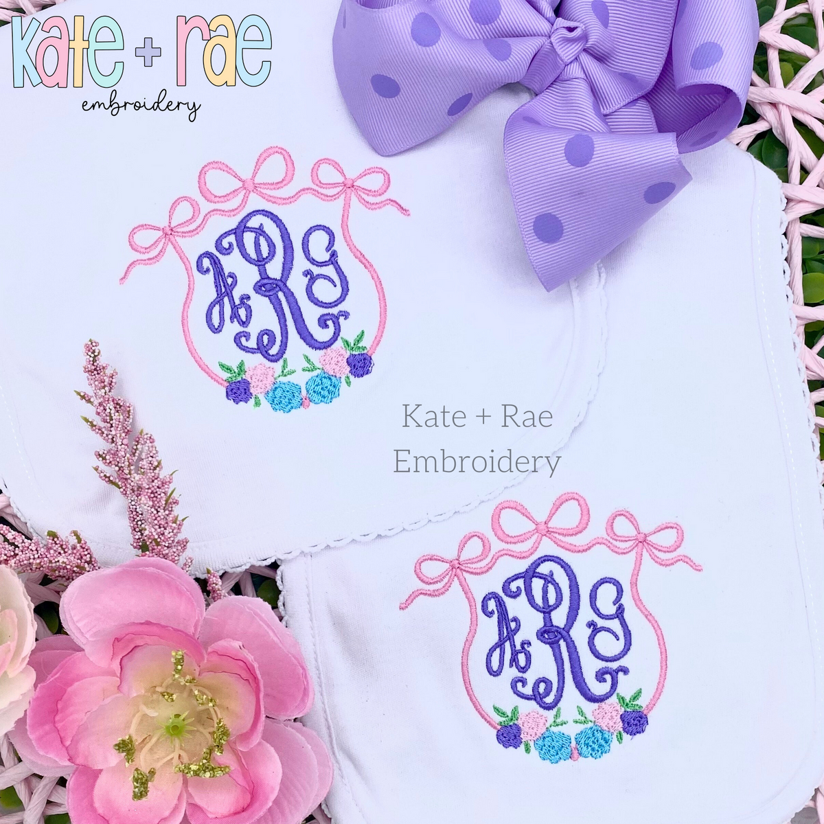 Floral Triple Flowy Bow Crest Embroidery Design: Two white baby items with pink triple bow frames and floral clusters around purple monograms
