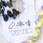 Girl's Mardi Gras Trio Sketch Stitch Embroidery Design: Mardi Gras beads, mask, and fleur de lis in sketch stitch above the name Veronica on a white ruffled bib