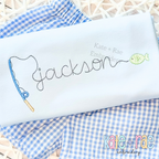Gone Fishing Bean Stitch Embroidery Font: The name jackson in gray bean stitch script with a blue fishing pole and fish on a light blue shirt