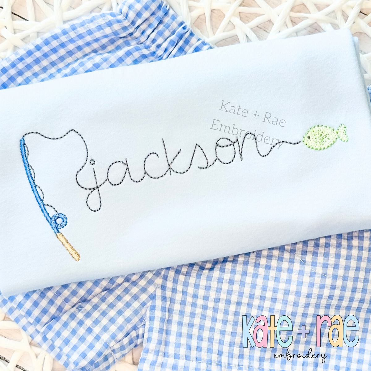 Gone Fishing Bean Stitch Embroidery Font: The name jackson in gray bean stitch script with a blue fishing pole and fish on a light blue shirt