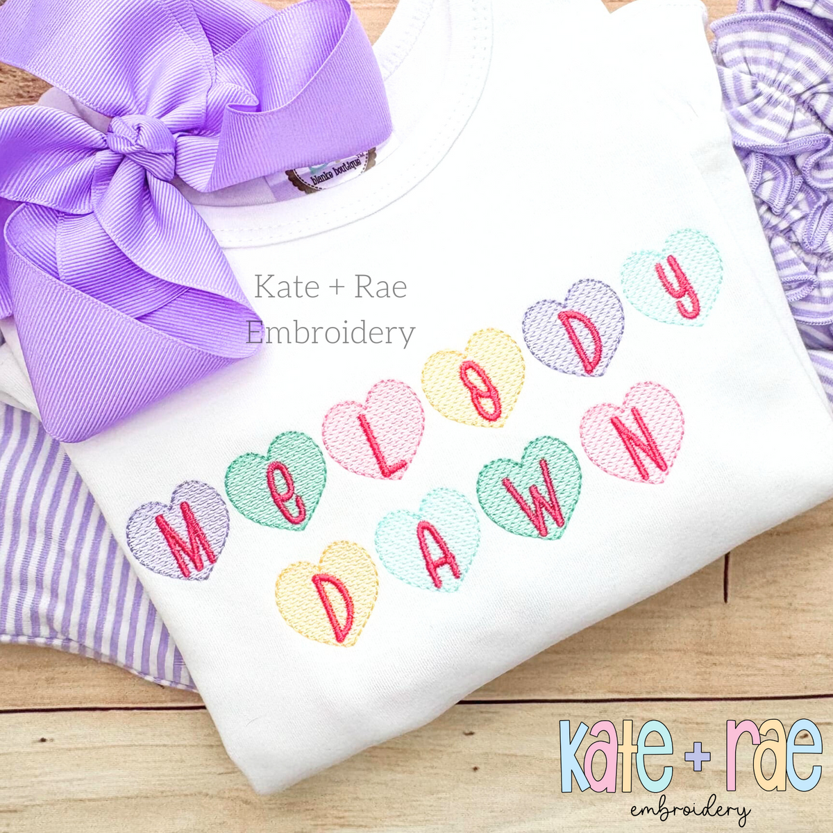 Candy Heart Sketch Stitch Embroidery Font: Pastel candy hearts with pink letters spelling Melody Dawn on a white shirt