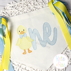 Boys One Lucky Duck with Bow Tie #2 Sketch Stitch Embroidery Design: Yellow sketch duck with a blue bow tie beside one in blue script on a pennant banner with ribbons