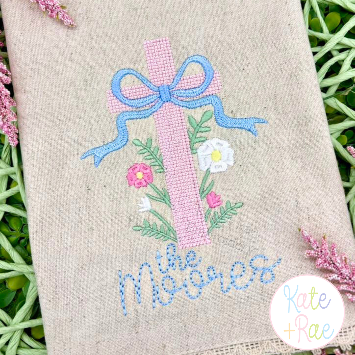 Cross Stitch Floral Cross Embroidery Design: Pink cross stitch floral cross with a blue bow above the Moores on a linen towel