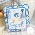 Girl Goose Mini Fill with Bow Embroidery Design: White goose with a blue bow and the name Opal in blue on a scalloped door hanger