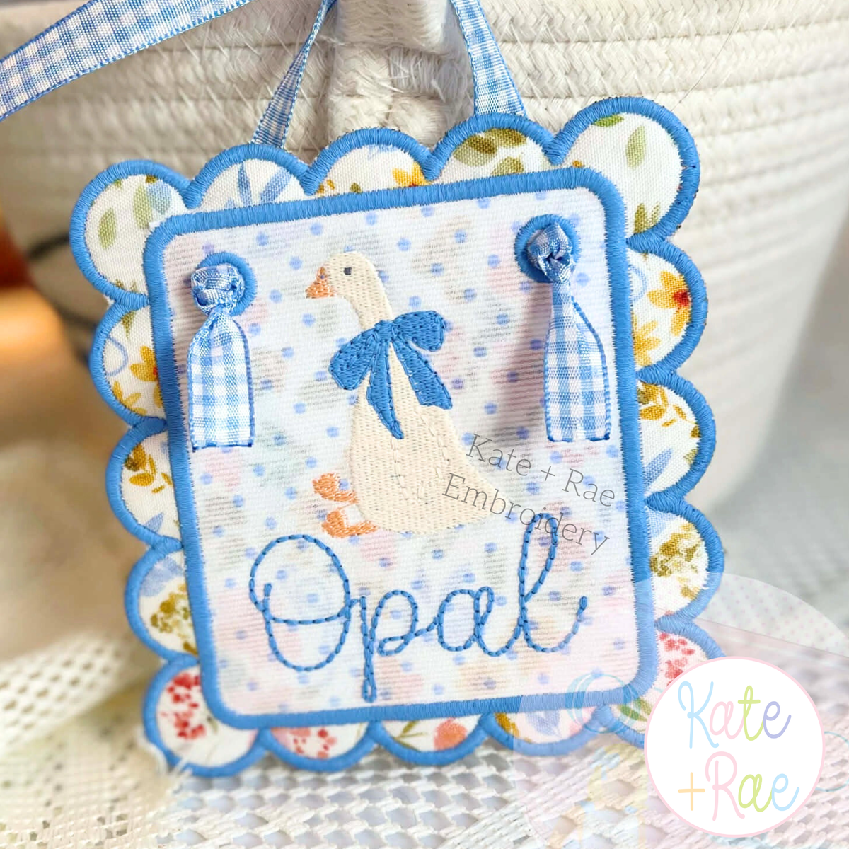 Girl Goose Mini Fill with Bow Embroidery Design: White goose with a blue bow and the name Opal in blue on a scalloped door hanger