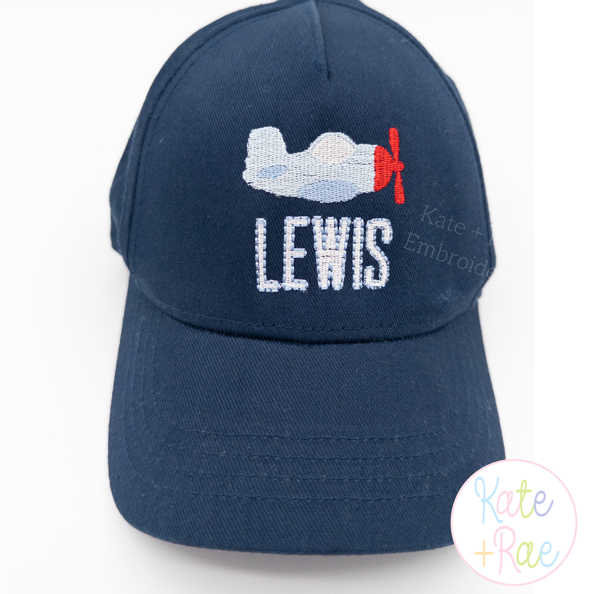 Airplane Mini Fill Stitch Embroidery Design: Mini airplane above LEWIS in white letters on a navy baseball cap