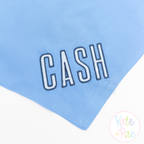 Beau Fill Stitch with Satin Border Embroidery Font: The name CASH in white fill stitch letters with navy border on a light blue blanket