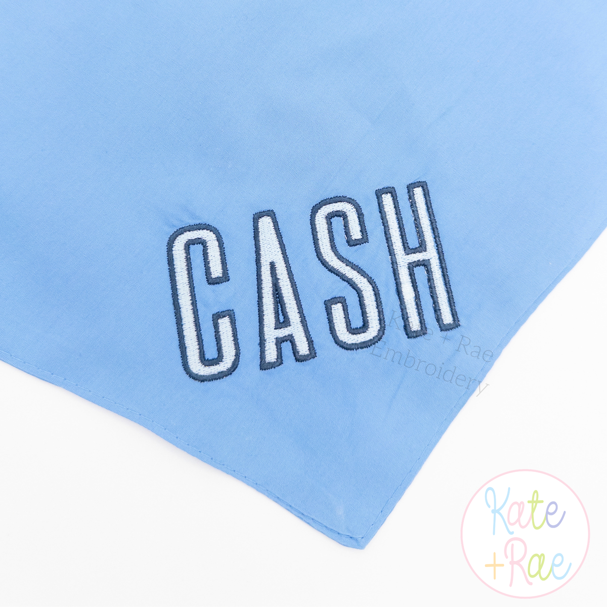 Beau Fill Stitch with Satin Border Embroidery Font: The name CASH in white fill stitch letters with navy border on a light blue blanket