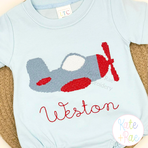 Airplane Cross Stitch Embroidery Design: Cross stitch airplane above the name Weston in red script on a light blue shirt