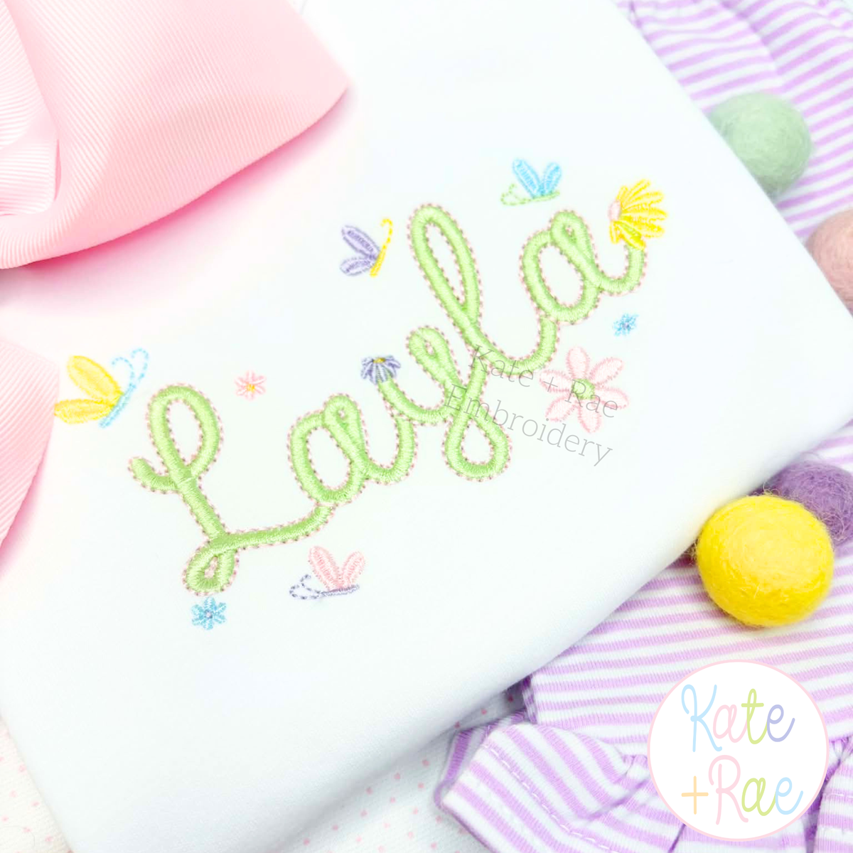 Tiny Spring Flowers and Butterfly Satin Stitch Mini Embroidery Design: The name Layla in green outline script with tiny flowers and butterflies on a white shirt