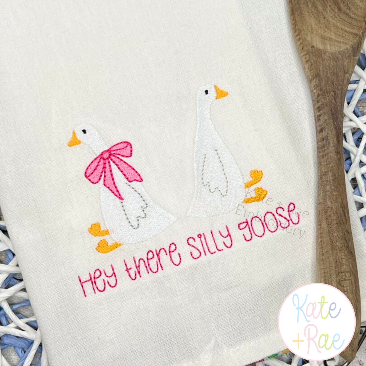 Goose Mini Fill Embroidery Design: White mini fill geese, one with a pink bow, above Hey there silly goose on a tea towel