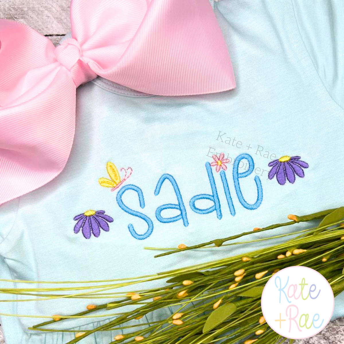 Tiny Spring Flowers and Butterfly Satin Stitch Mini Embroidery Design: The name Sadie in blue with tiny purple flowers on a light blue shirt