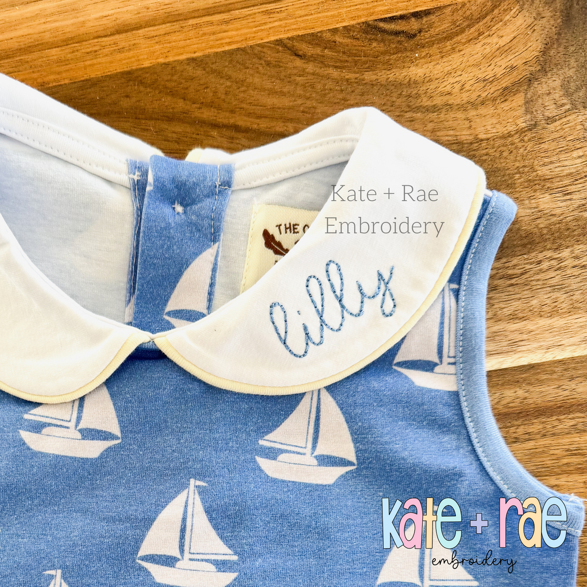 Hello Bean Stitch Embroidery Font: The name lilly in light blue script stitched on the white collar of a blue sailboat print dress