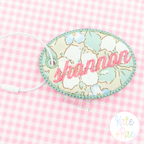 Oval Satin Stitch Bag Tag/ Keychain In The Hoop Embroidery Design: Floral oval bag tag with shannon in pink script on pink gingham