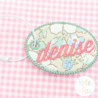 Oval Satin Stitch Bag Tag/ Keychain In The Hoop Embroidery Design: Floral oval bag tag with denise in pink script on pink gingham