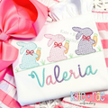 Girl's Easter Bunny with Carrots Trio Cross Stitch Embroidery Design: Three aqua, pink, and purple cross stitch bunnies with bows above the name Valeria in pastel script on a white shirt