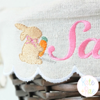 Girl's Easter Bunny with Carrot and Bow Mini Fill Stitch Embroidery Design: Close-up of a tan mini bunny with a pink bow and carrot beside the name Sadie in pink script on a basket liner