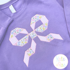 Quilt Block Bow Zigzag Applique Embroidery Design: Pink and blue floral quilt block bow applique on a purple sweatshirt