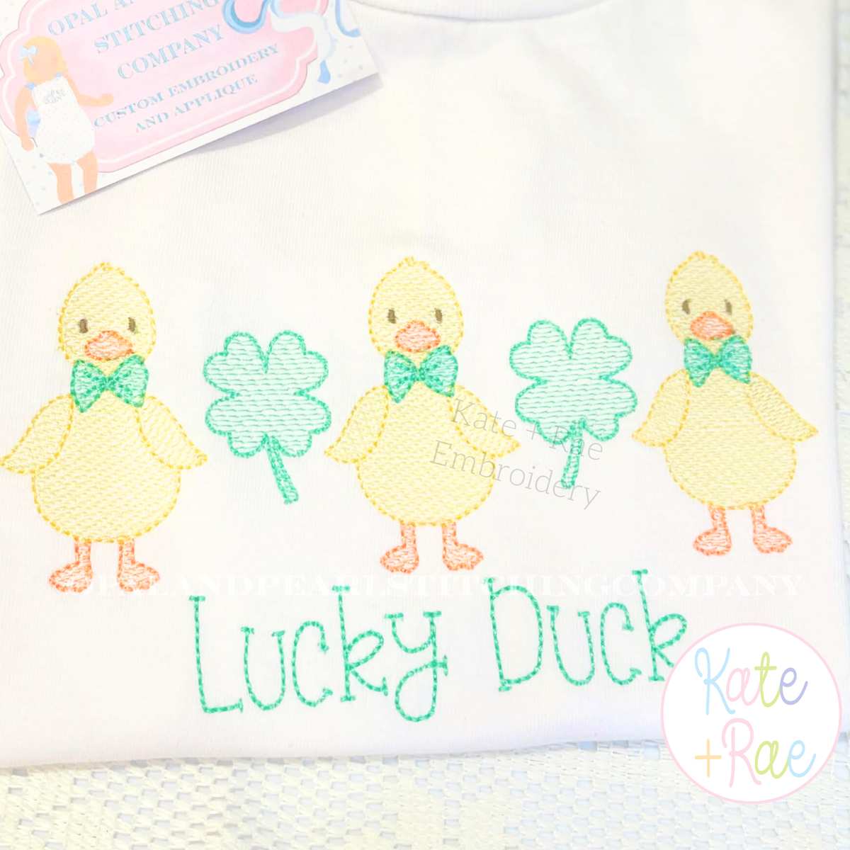 Duck with Bow Tie Sketch Stitch Embroidery Design: Three sketch ducks with green bow ties between shamrocks above Lucky Duck in green on a white shirt