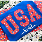 Curved USA with Bow Zigzag Stitch Applique Embroidery Design: USA in red floral zigzag applique letters with a white bow on a royal blue shirt