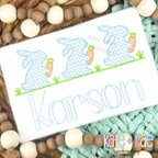 Boy's Easter Bunny with Carrots Trio Cross Stitch Embroidery Design: Three light blue cross stitch bunnies holding carrots above the name Karson in blue sketch letters on a white shirt