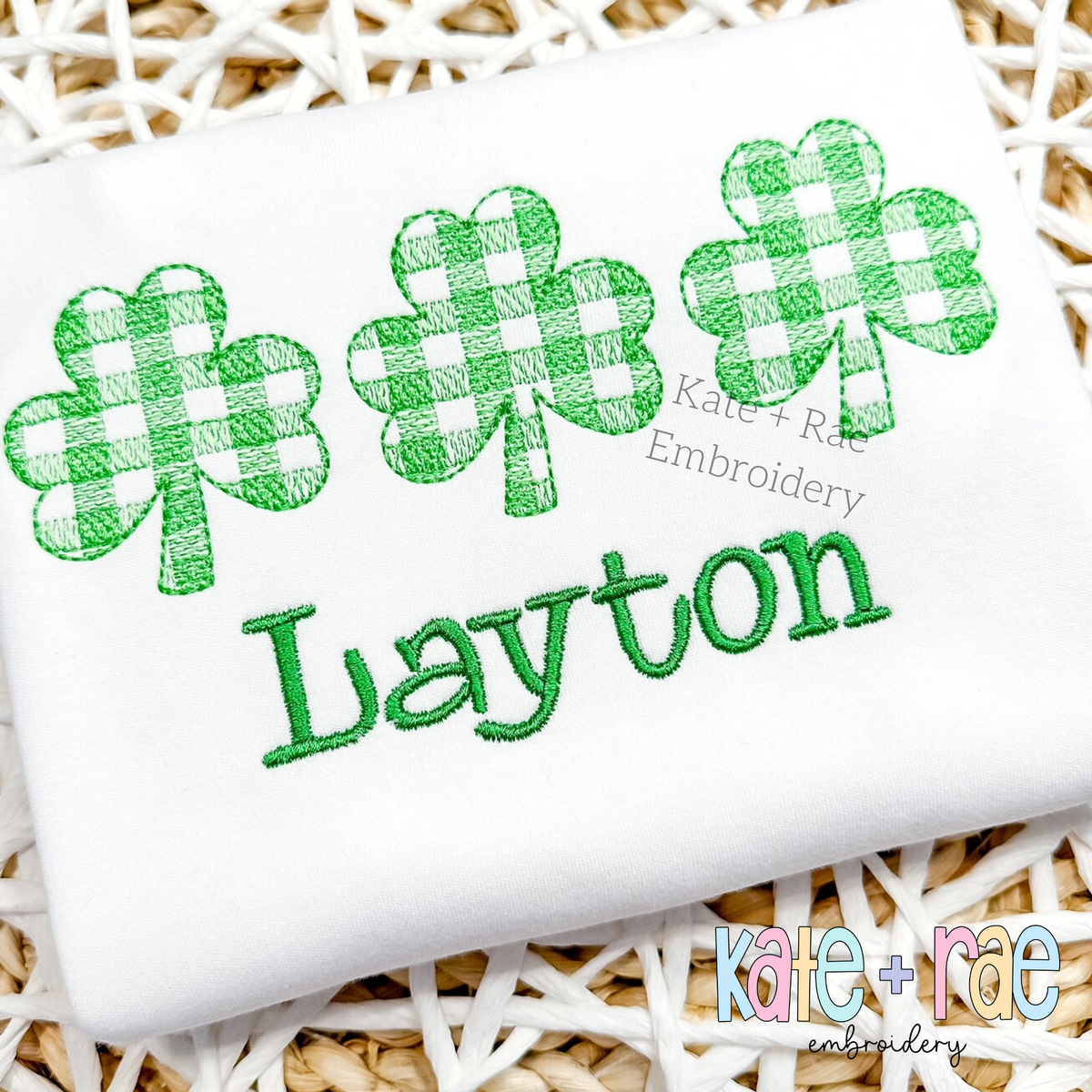 Plaid Shamrock Trio Sketch Stitch Embroidery Design: Three green gingham sketch stitch shamrocks above the name Layton in green on a white shirt