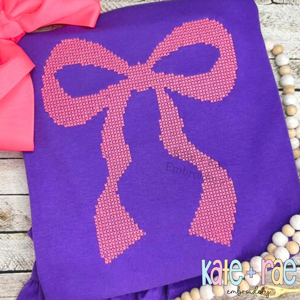 Merritt Bow Cross Stitch Embroidery Design: Pink cross stitch Merritt bow on a purple shirt