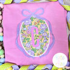 Oval Monogram Frame with Long Tail Bow Satin Applique Embroidery Design: Lavender bow oval frame around a purple floral applique with a pink letter C on a pink shirt