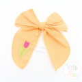 Spring Tulip Mini Fill Stitch Embroidery Design: Small pink tulip stitched on the tail of an orange fabric hair bow
