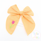 Spring Tulip Mini Fill Stitch Embroidery Design: Small pink tulip stitched on the tail of an orange fabric hair bow