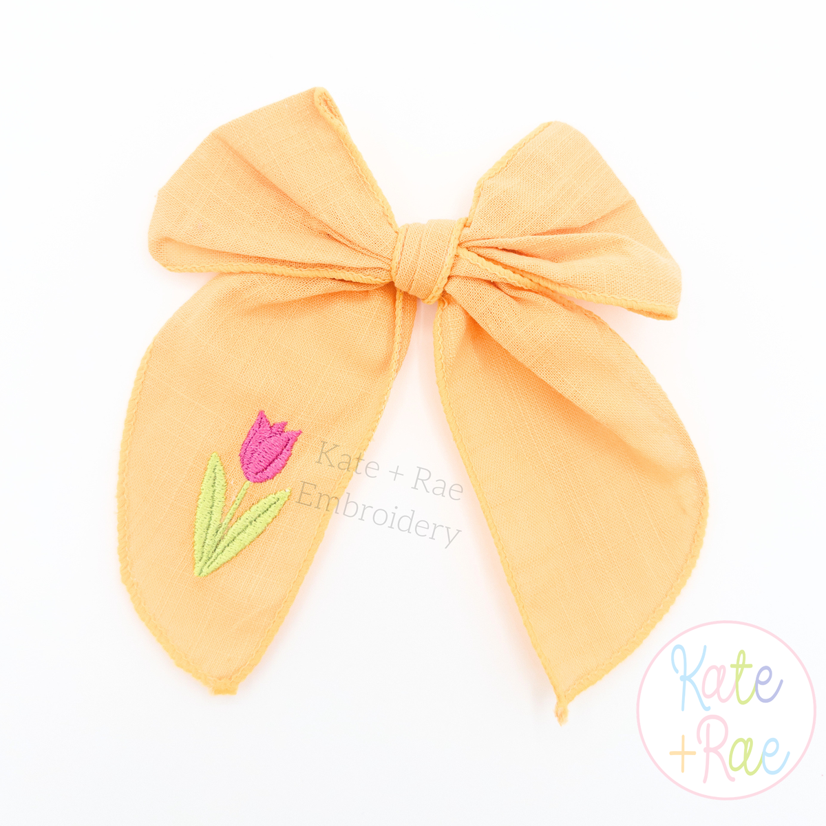 Spring Tulip Mini Fill Stitch Embroidery Design: Small pink tulip stitched on the tail of an orange fabric hair bow