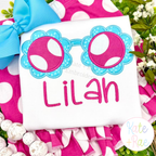 Flower Sunglasses Satin Applique Embroidery Design: Aqua flower shaped sunglasses with pink polka dot lenses above the name Lilah in pink on a white shirt