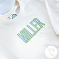 Beau Fill Stitch with Satin Border Embroidery Font: The name MILLER in green and blue fill stitch letters with satin border on a cream sweatshirt