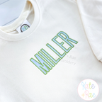 Beau Fill Stitch with Satin Border Embroidery Font: The name MILLER in green and blue fill stitch letters with satin border on a cream sweatshirt