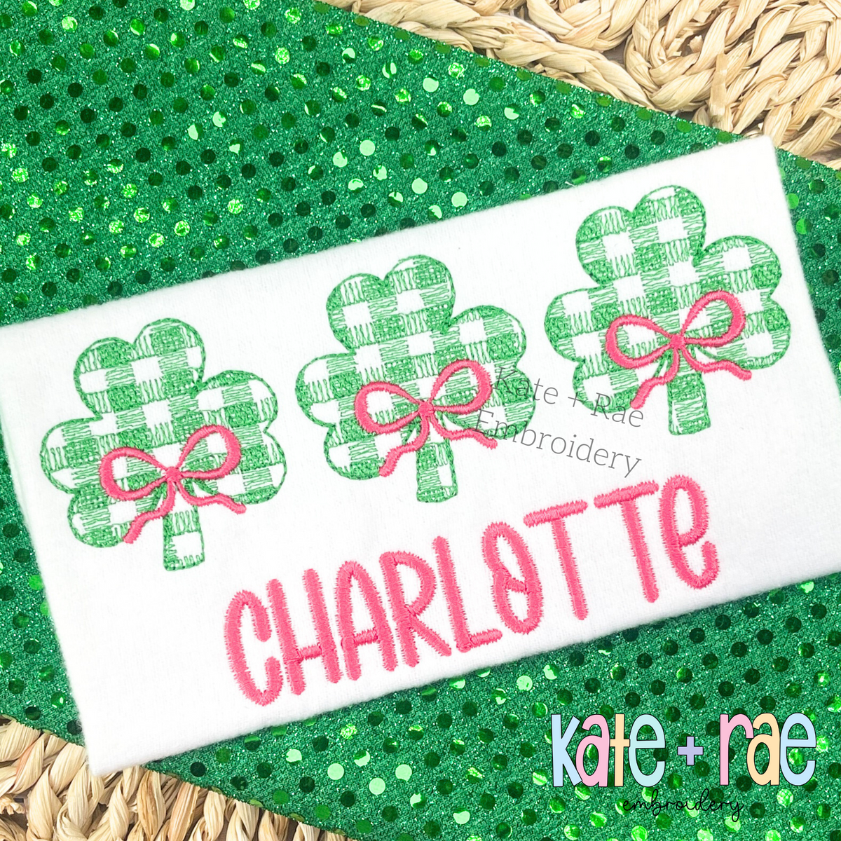 Plaid Shamrock Trio with Bows Sketch Stitch Embroidery Design: Three green gingham shamrocks with pink bows above the name CHARLOTTE in pink on a white shirt