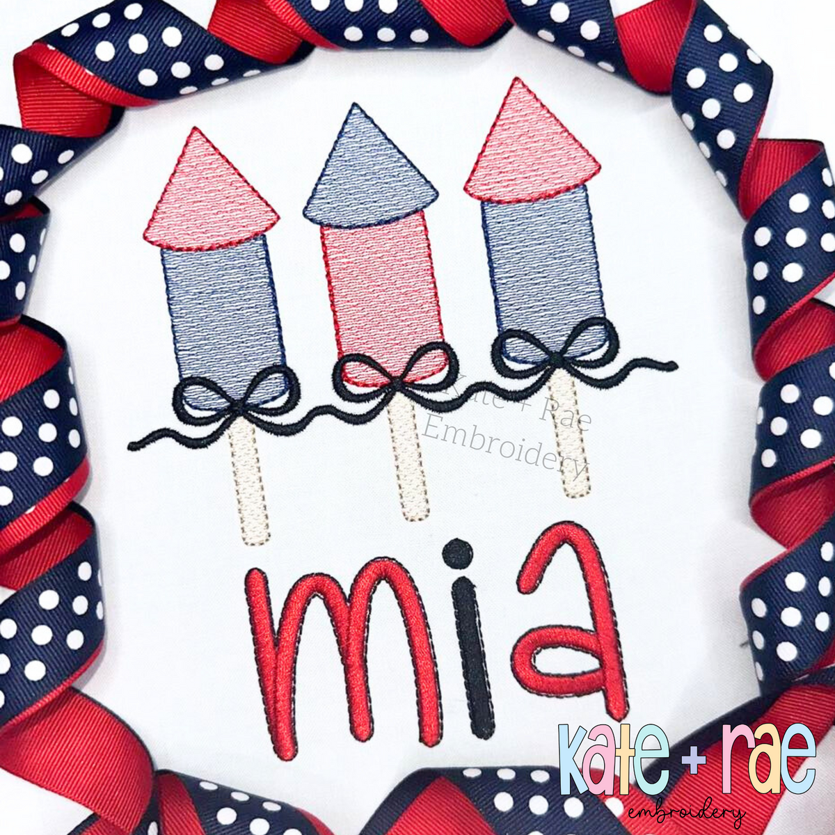 Girl's Firework Trio with Bows Sketch Stitch Embroidery Design: Three red and blue sketch firework rockets with navy bows above the name mia in red on a white shirt