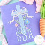 Floral Cross Pattern Fill Stitch Embroidery Design: Light blue floral cross with a bow above an SSA monogram on a lavender sweatshirt