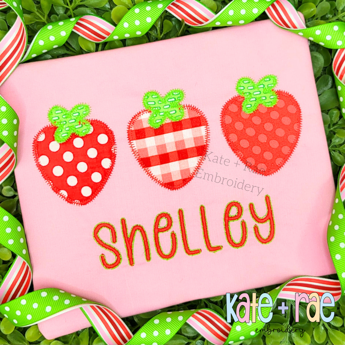Three polka dot, gingham, and dotted strawberry appliques above the name Shelley on a pink shirt