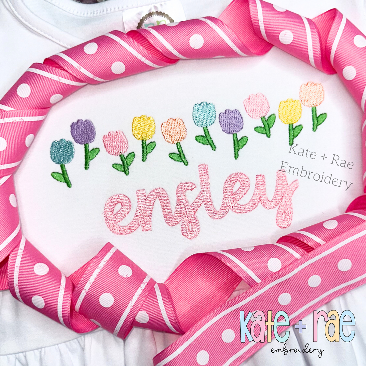 Tulip Party Fill Stitch Embroidery Design: Row of pastel fill stitch tulips above the name ensley in pink glitter letters on a white shirt