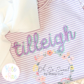 Delilah Two Toned Satin Stitch Embroidery Font: The name tilleigh in two toned lavender and aqua satin script on a striped shirt