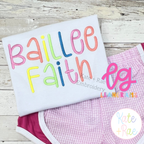 Happy Days Satin Stitch Embroidery Font: The name Baillee Faith in pastel satin stitch letters on a white shirt with pink gingham shorts